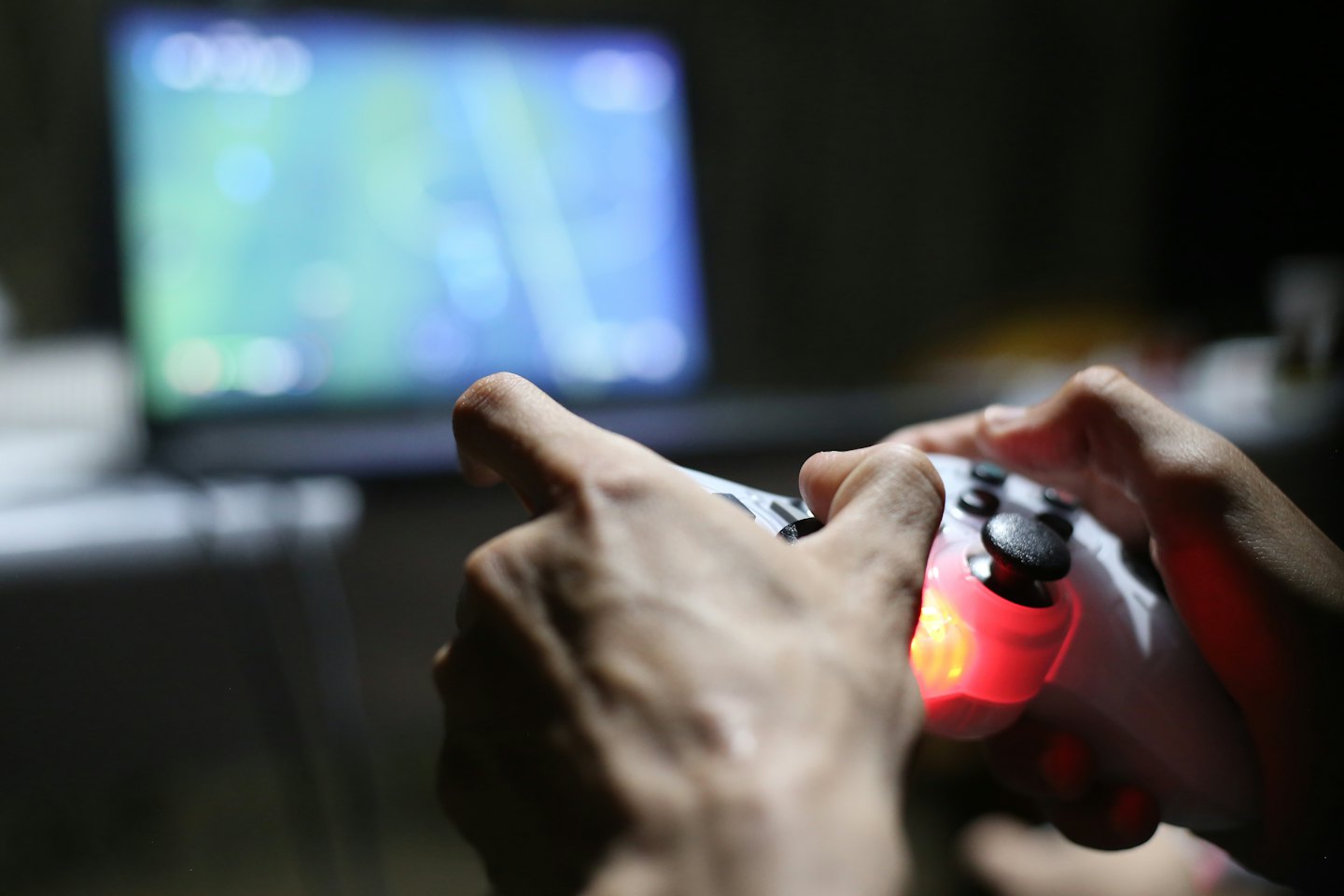 Hands holding a video game controller with a glowing red light.